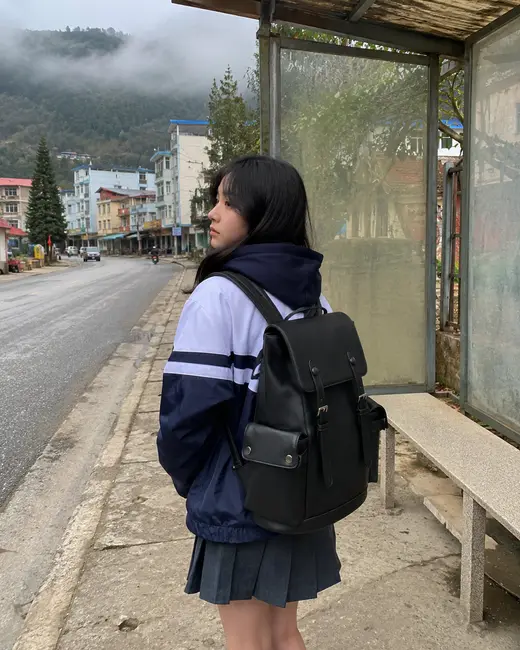 Bạn nữ đeo balo Guardian màu đen đứng chờ ở trạm xe buýt