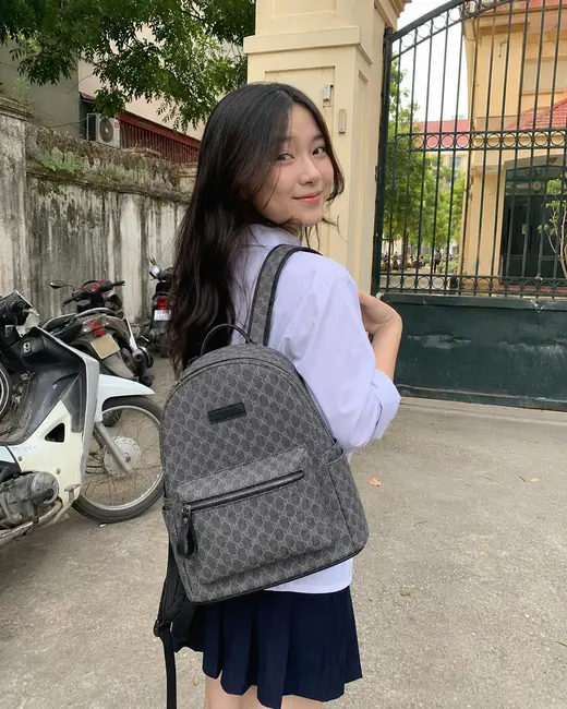 Bạn nữ đeo balo Scholar Daily họa tiết monogram xám trước cổng trường